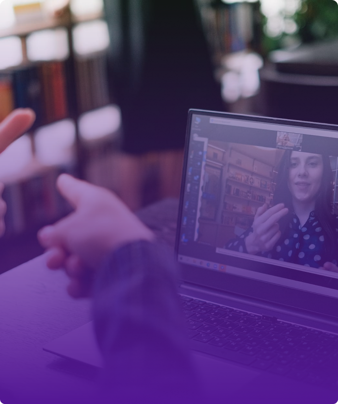 There is a photo of 2 people speaking in sign language on the computer. At the computer is a woman with long dark hair and white circles on her black shirt.